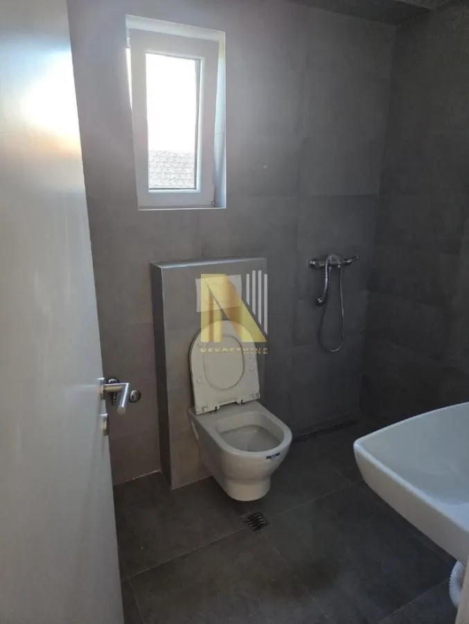 Manje kupatilo sa tamnim pločicama, wc šoljom i umivaonikom.