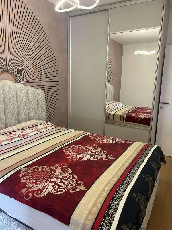 Namještena spavaća soba sa bračnim krevetom i velikim ugradnim ormarom sa ogledalom.