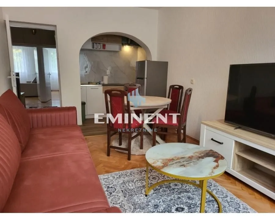 Living room with a sofa, TV, and dining table in the background.