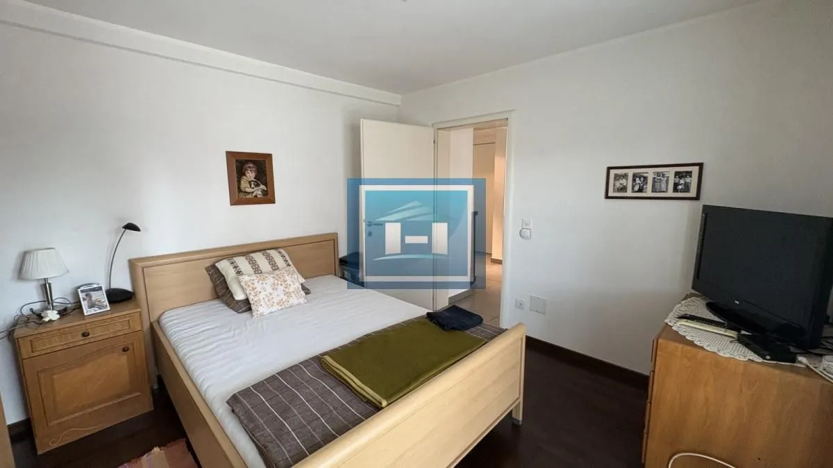 Nameštena spavaća soba sa bračnim krevetom, noćnim stočićem i televizorom.