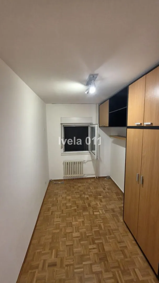Manja soba sa drvenim ormarima, parketom i prozorom.
