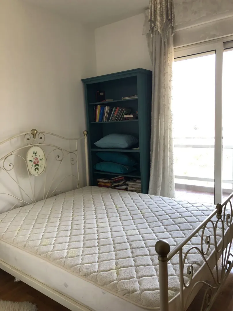 Bedroom with a metal bed and a bookshelf next to balcony doors.