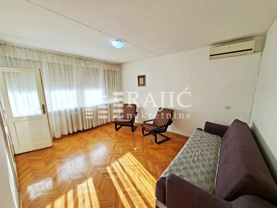 Living room with parquet flooring, seating furniture, and double windows with curtains.