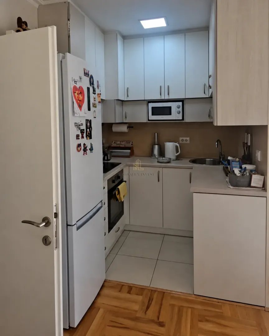 Manja kuhinja sa bijelim elementima, frižiderom i ugradnom rernom.