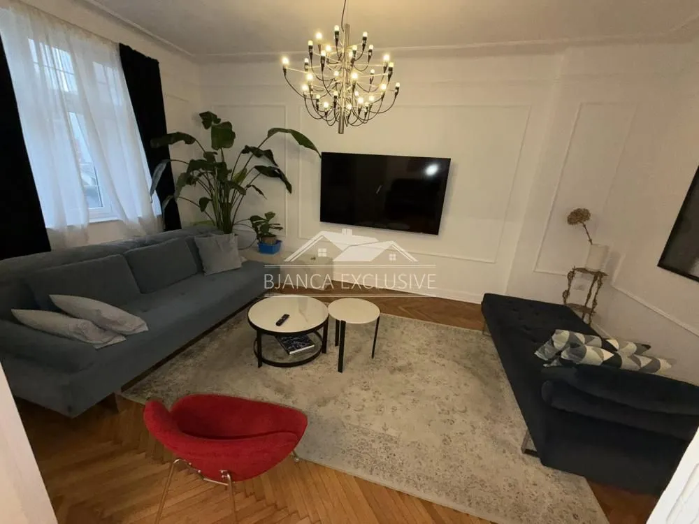 Dnevna soba sa garniturom, TV-om i trpezarijskim stolom.