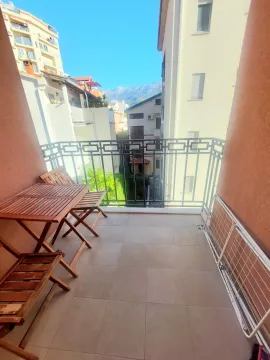 Small furnished balcony with a wooden table and chairs and a view of surrounding buildings. - image 20