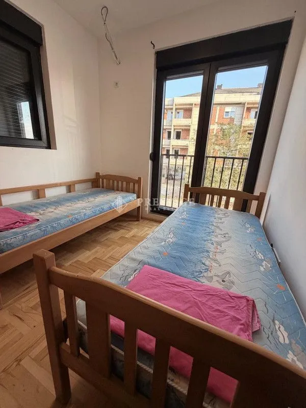 Spavaća soba sa dva drvena kreveta i izlazom na balkon.