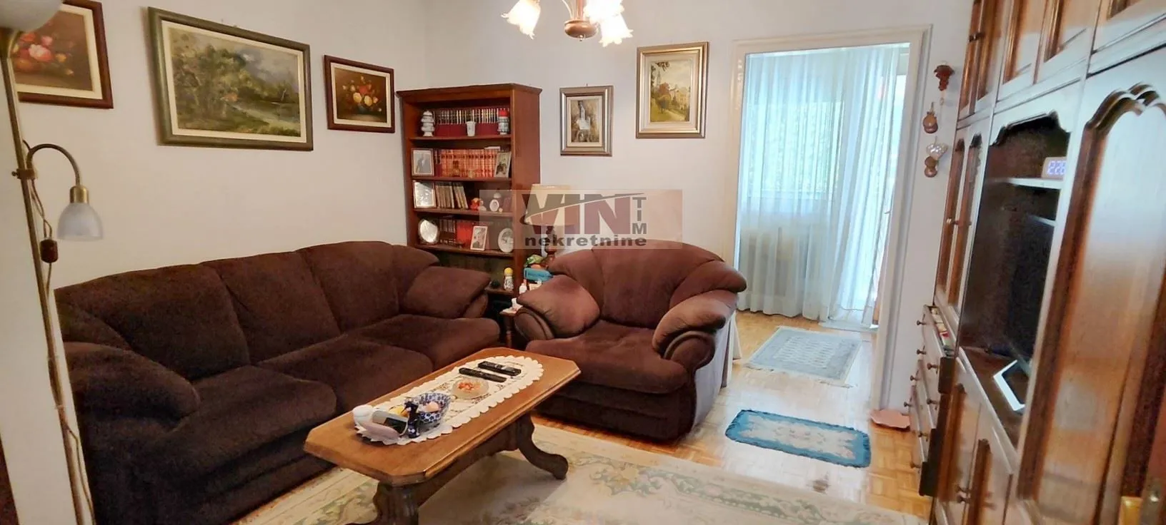 Dnevna soba sa garniturom za sedenje, drvenim nameštajem i slikama na zidu.