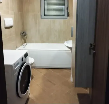 Smaller bathroom with a bathtub, washbasin, and washing machine. - image 10