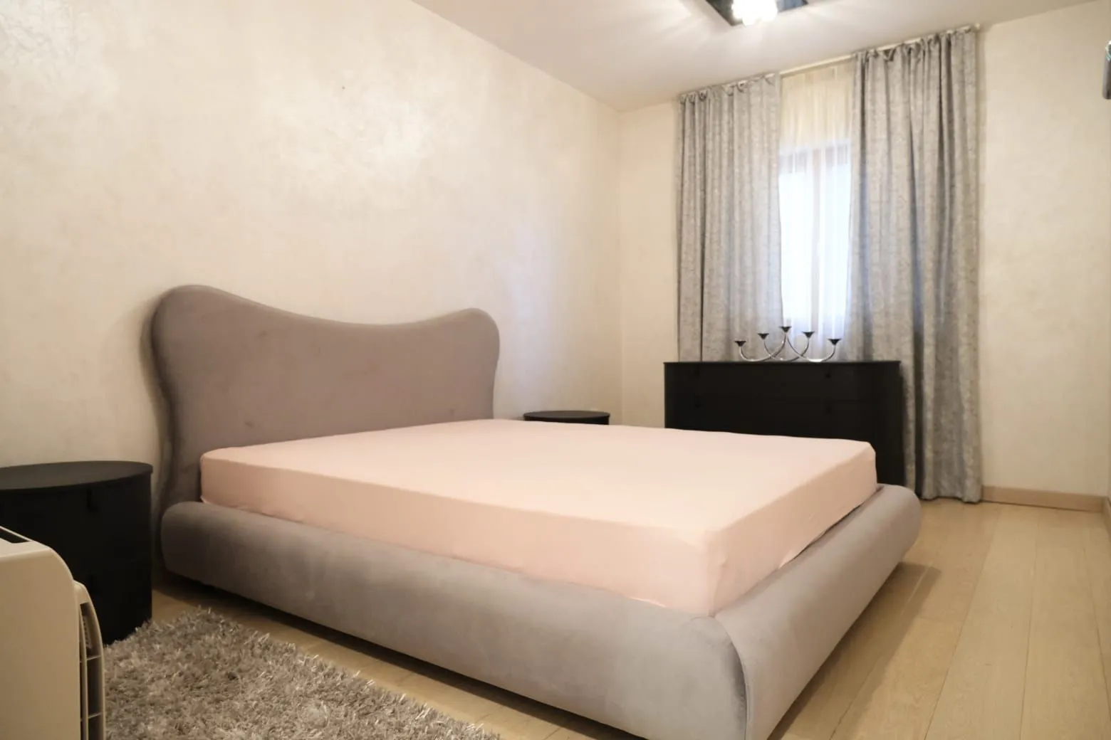 Bright bedroom with a large grey bed and a chest of drawers near the window.