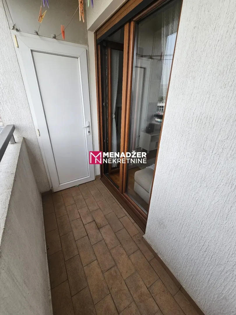 Nabrana balkonska terasa sa popločanim podom i vratima koja vode u unutrašnjost.