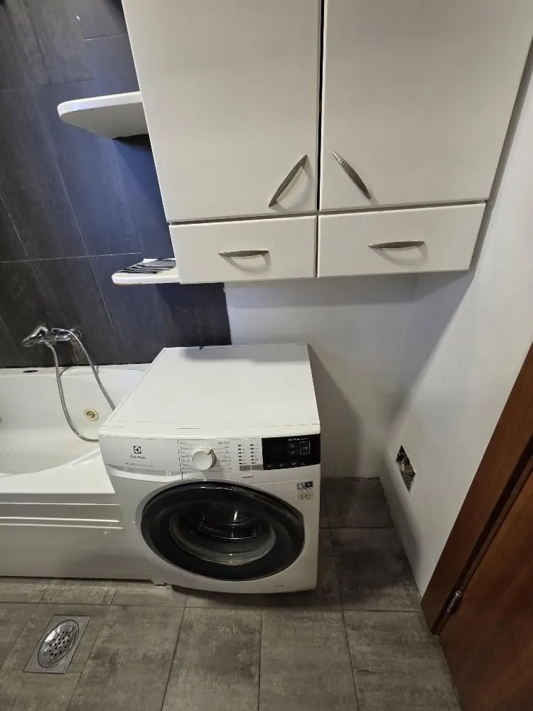 Bathroom equipped with a bathtub, washing machine, and white wall cabinets.