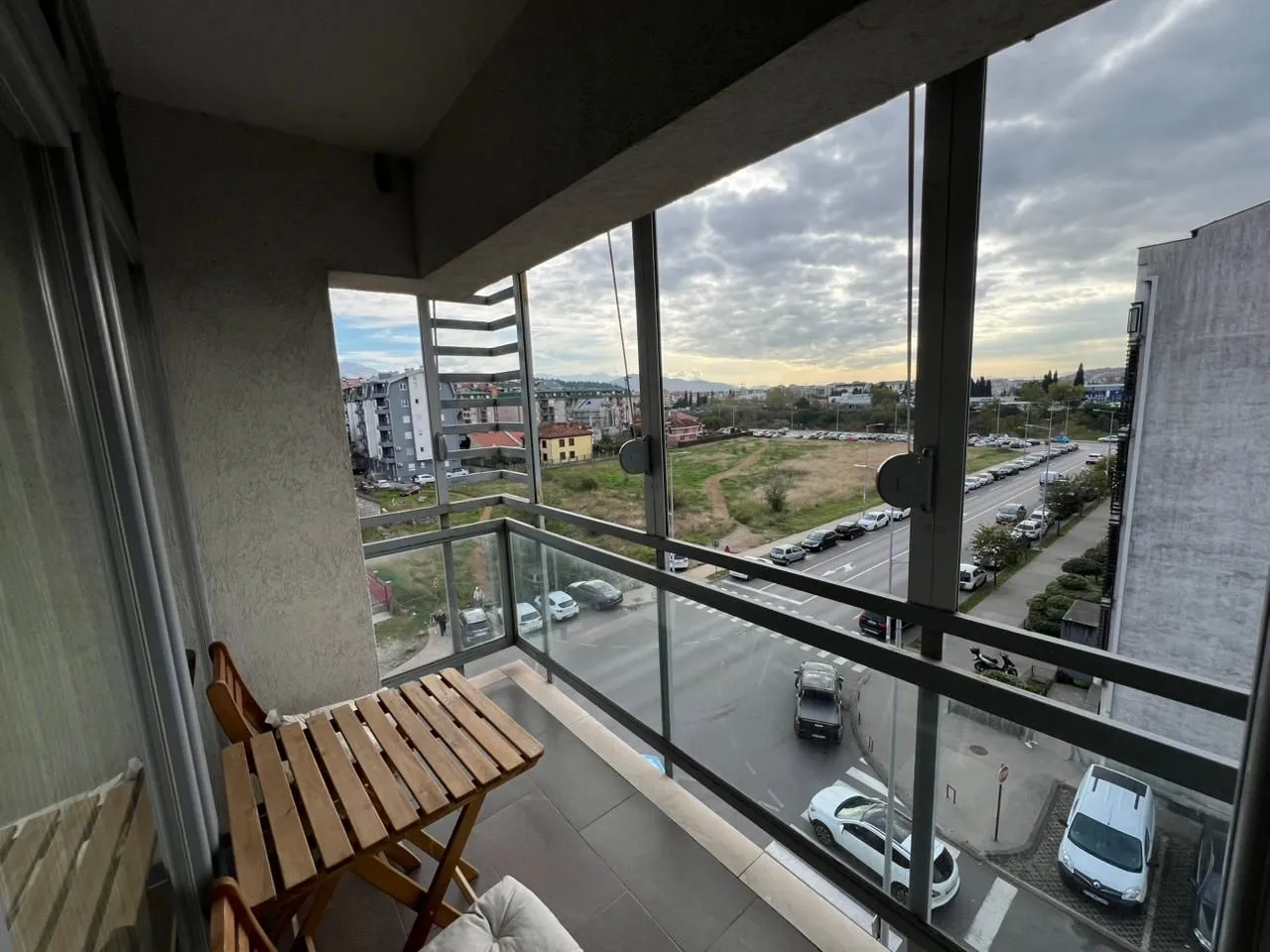 Zastakljeni balkon sa malim drvenim stočićem i pogledom na ulicu.