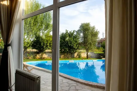 View through the window towards a courtyard with a swimming pool and greenery. - image 2