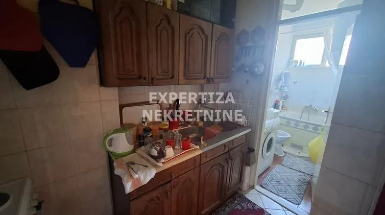 Starija kuhinja sa drvenim elementima i neredom na radnoj površini.