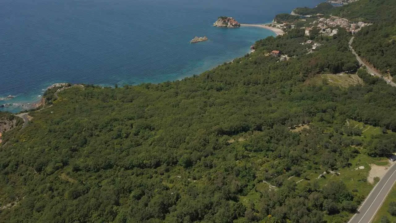Pogled iz vazduha na obalu mora, zelenilo i ostrvo u daljini.