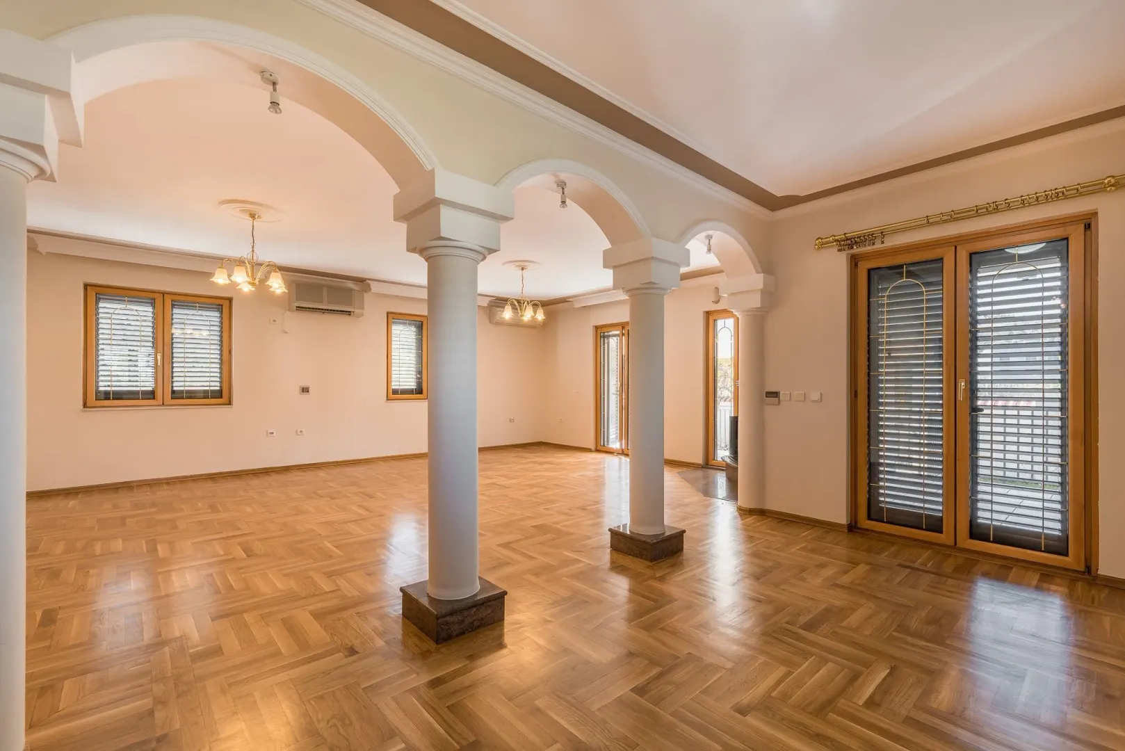 Spacious empty room with decorative columns and wooden parquet flooring.