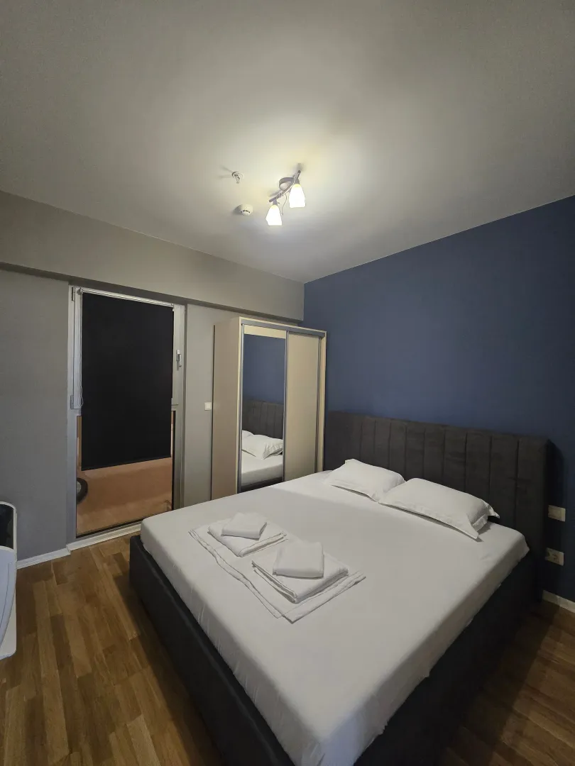 Uređena spavaća soba sa bračnim krevetom, ormarom i izlazom na terasu.