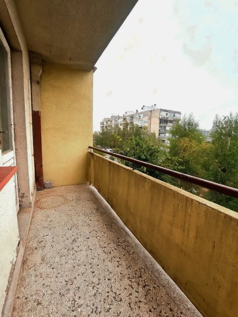 Natkriveni balkon sa pogledom na okolne zgrade i zelenilo.