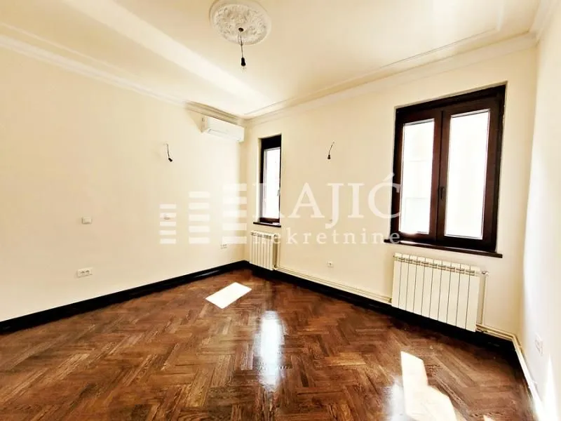 Empty room with parquet flooring and windows.