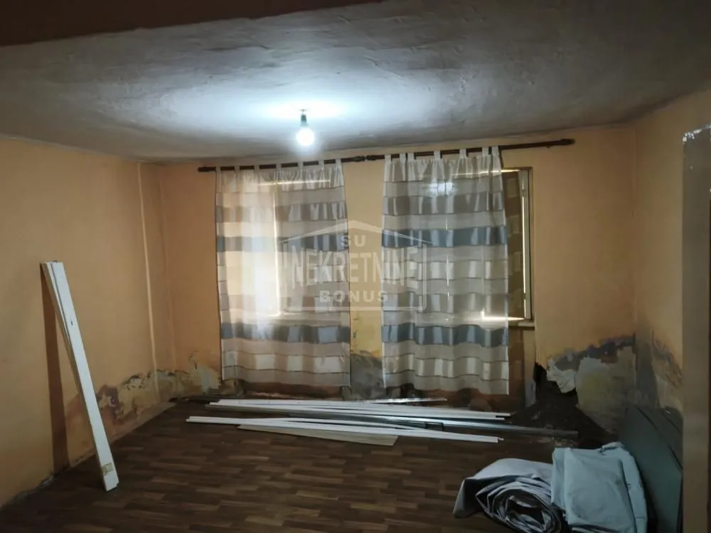 Prazna prostorija sa prozorom i oštećenim zidovima.