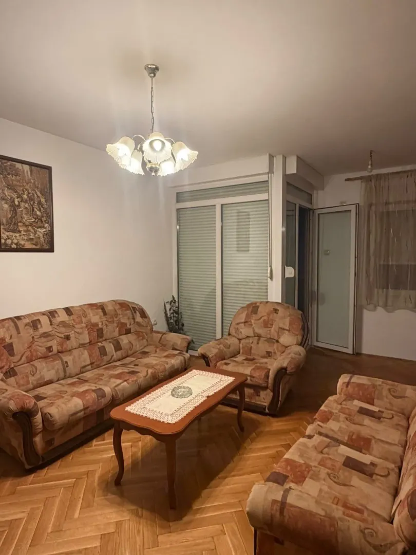 Dnevna soba sa garniturom za sedenje, stočićem i drvenim parketom.