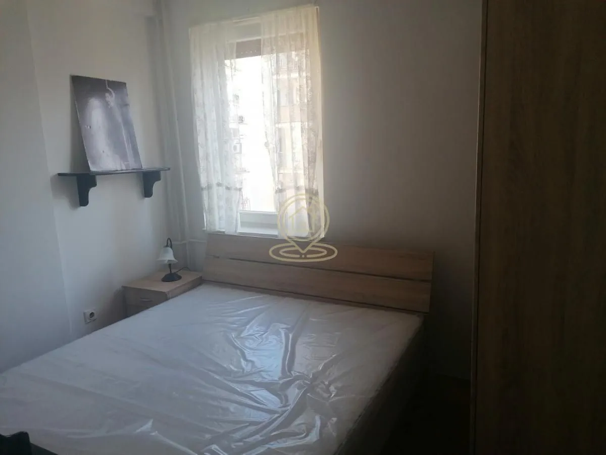 Manja spavaća soba sa bračnim krevetom, noćnim stočićem i prozorom.