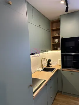 Moderna kuhinja sa zelenim elementima, drvenom radnom pločom i ugrađenim aparatima. - image 9