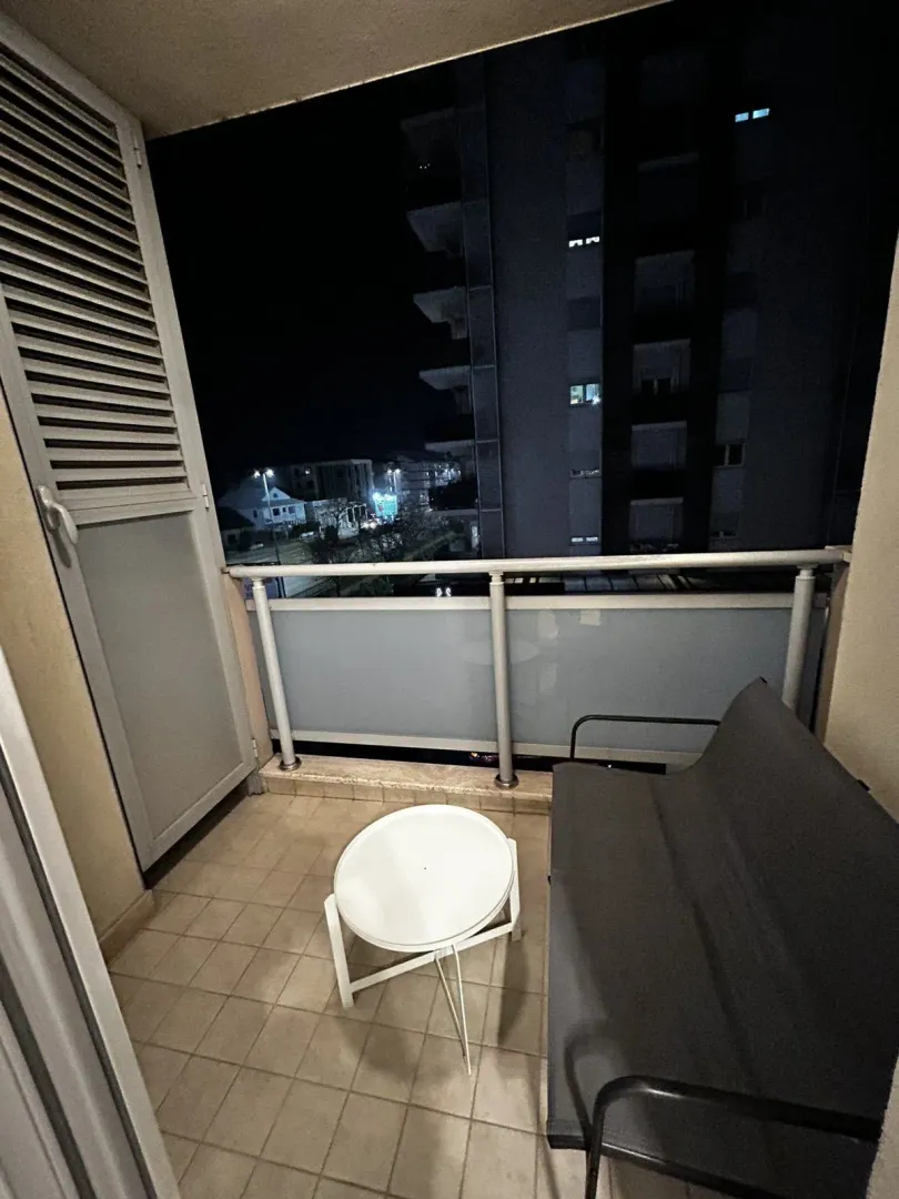 Small balcony with seating and a view of the city at night.