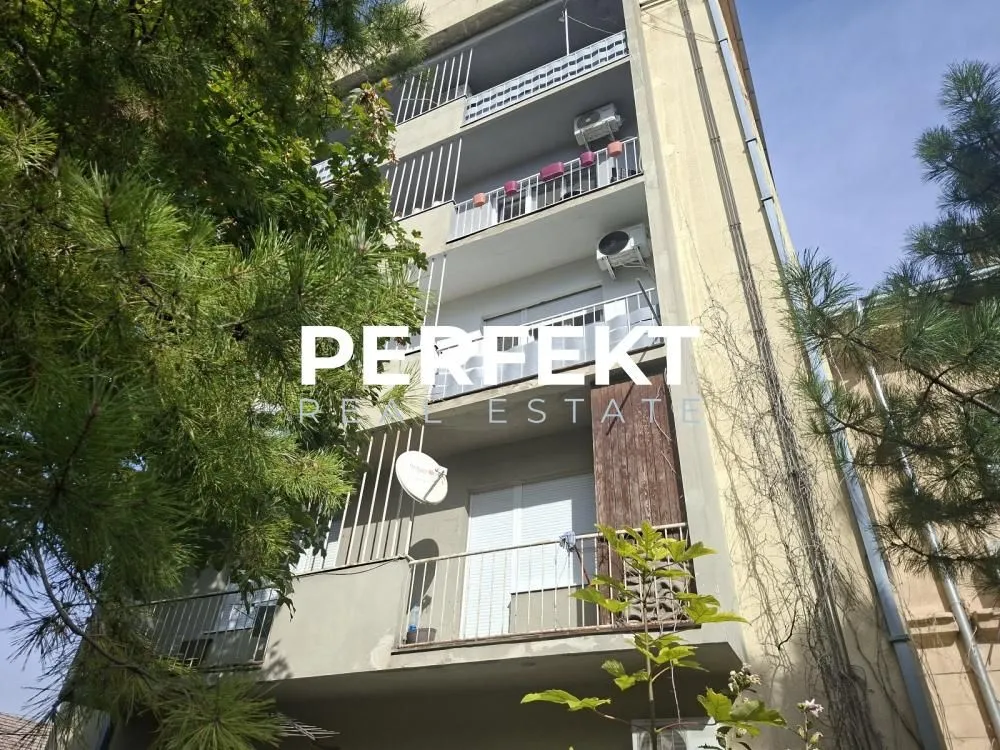 Spoljašnji izgled stambene zgrade sa balkonima okružen zelenilom.