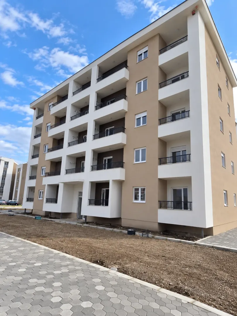Spoljašnji izgled moderne stambene zgrade sa terasama i uređenim dvorištem.