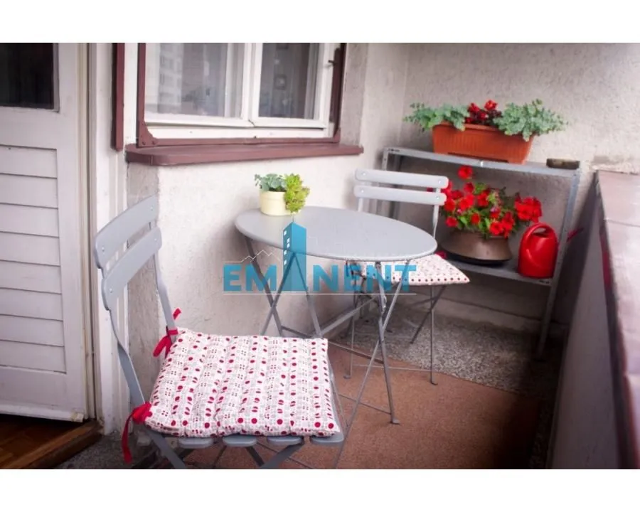 Small furnished balcony with a table, chairs, and flowers.