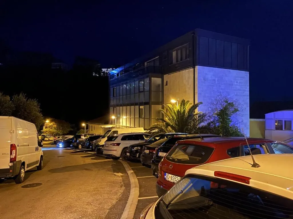Pogled na spoljašnjost zgrade i parking sa parkiranim automobilima noću.