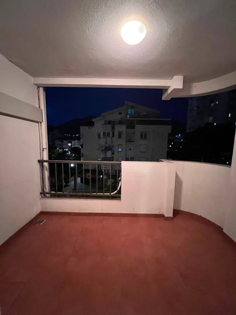 Prazna natkrivena terasa sa pogledom na okolne zgrade u noćnim uslovima.