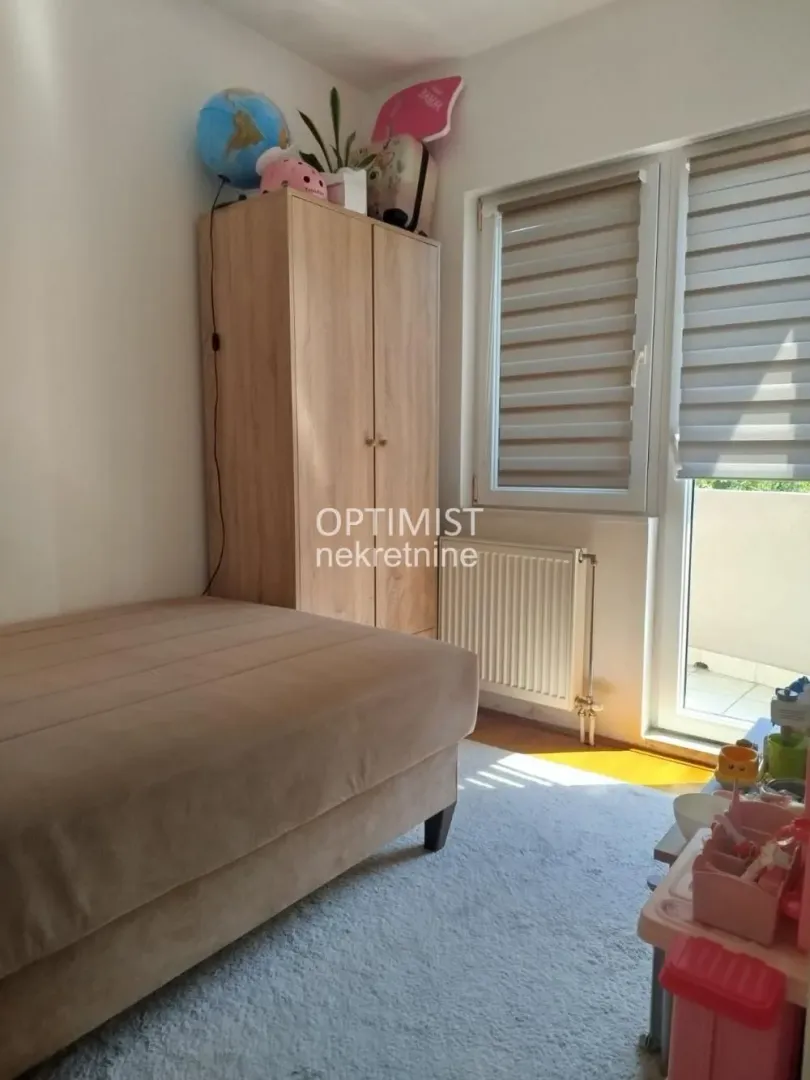 Nameštena spavaća soba sa krevetom, ormanom i izlazom na terasu.