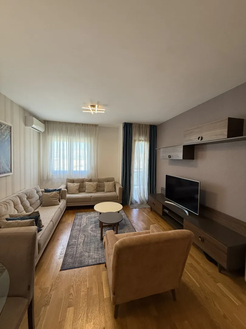 Dnevna soba sa garniturom, foteljom, TV komodom i tepihom.