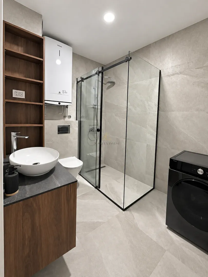 Modern bathroom with a walk-in shower, washbasin, and built-in washing machine.