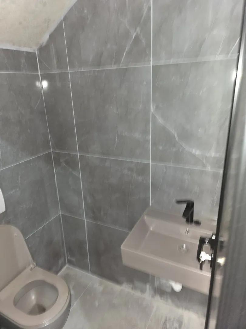 A small bathroom with grey tiles, a sink, and a toilet.