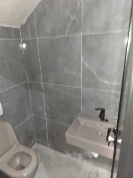 A small bathroom with grey tiles, a sink, and a toilet. - image 8