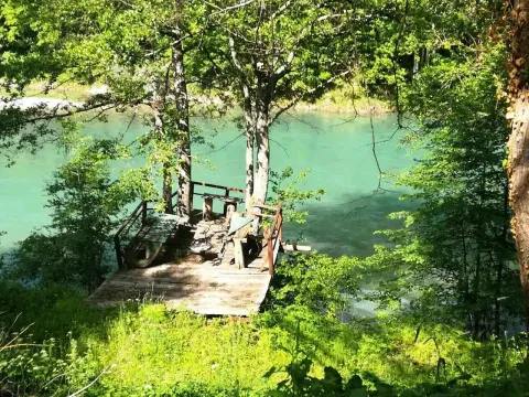 Drvena platforma sa klupama pored rijeke okružena bujnim zelenilom. - image 11