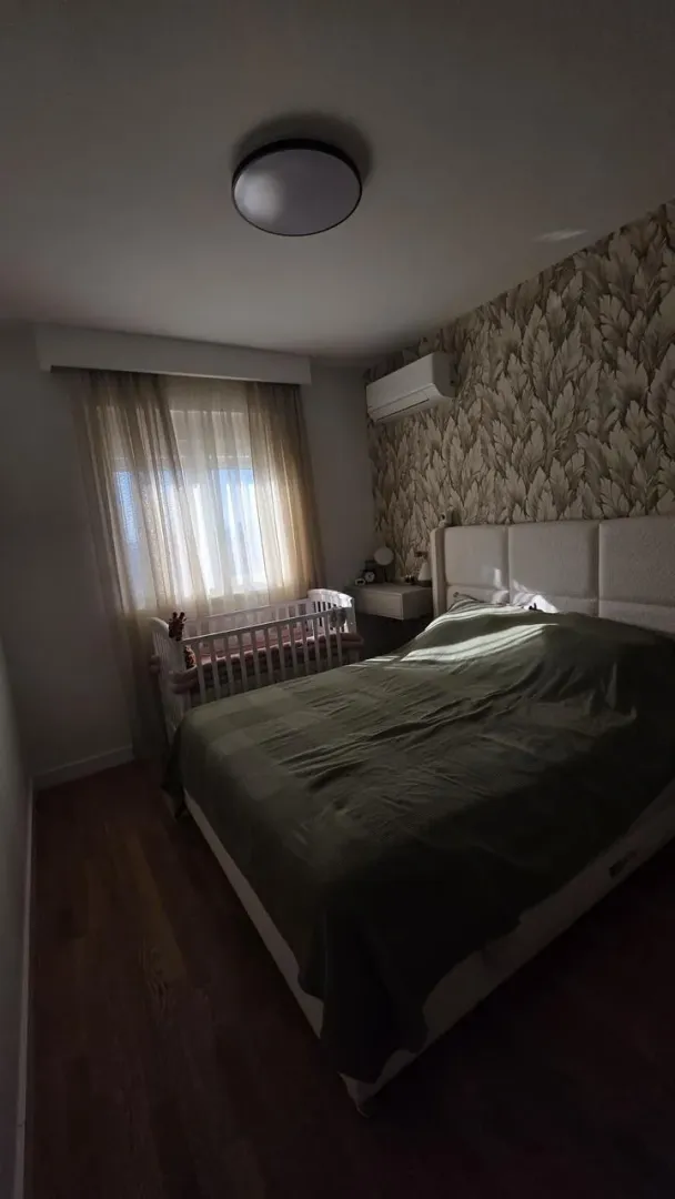 Spavaća soba sa bračnim krevetom i dječijim krevetcem pored prozora.
