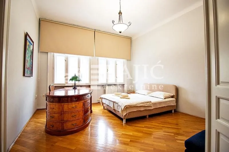 Spacious bedroom with a double bed, wooden flooring, and a large vintage desk.