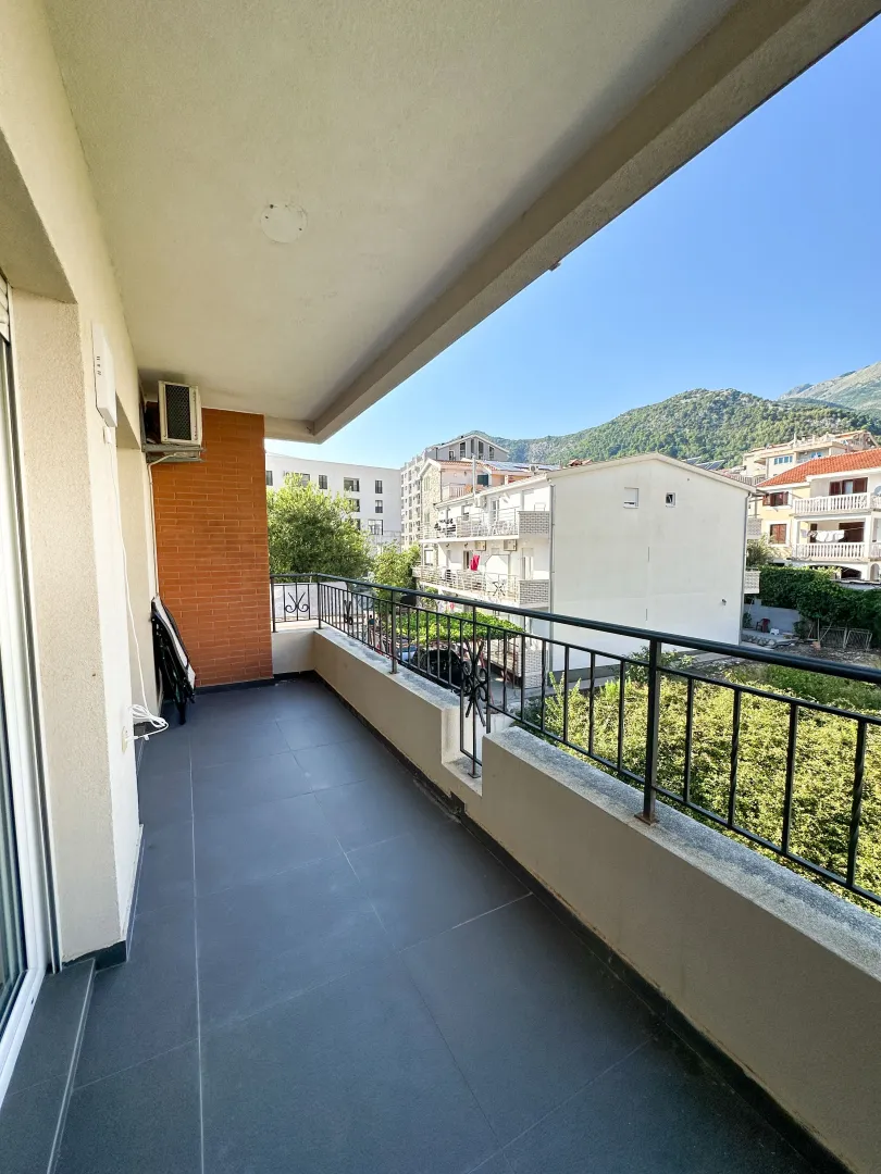Spacious balcony with a view of surrounding buildings and hills.