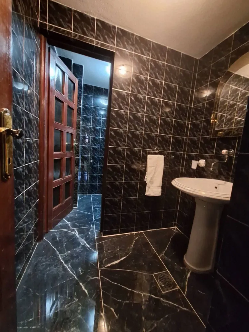 Bathroom tiled in dark tiles with a washbasin and a door.