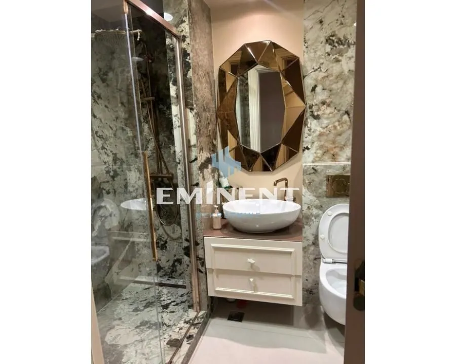 Luxuriously equipped bathroom with marble tiles, walk-in shower, and a unique mirror.