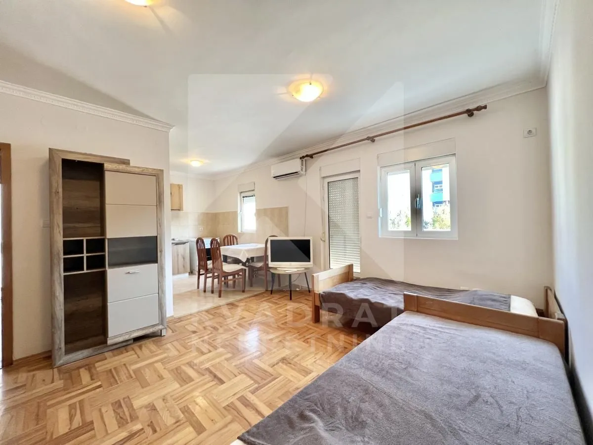 Living room with beds, wardrobe, and a kitchen in the background.