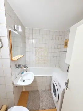 Manje kupatilo sa kadom, umivaonikom i veš mašinom obloženo svetlim pločicama. - image 10