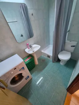 Smaller bathroom with a sink, shower cabin, toilet, and washing machine. - image 9