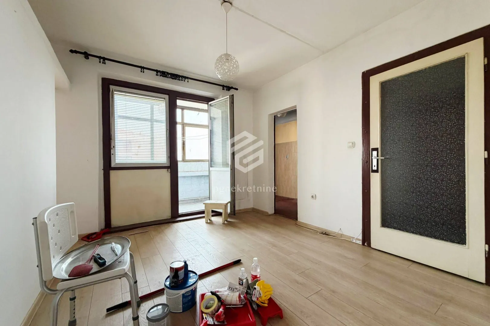 Prazna soba sa drvenim podom i izlazom na balkon tokom renoviranja.