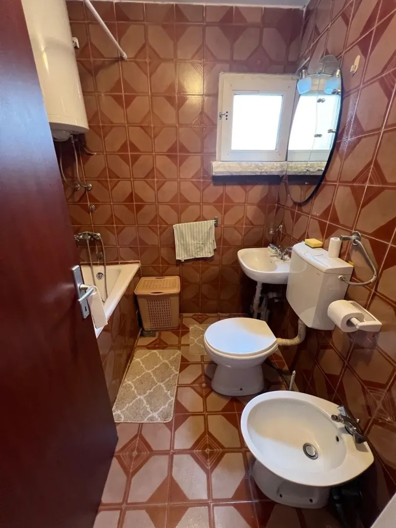 Manje kupatilo sa kadom, umivaonikom, toaletom i bideom u braon pločicama.